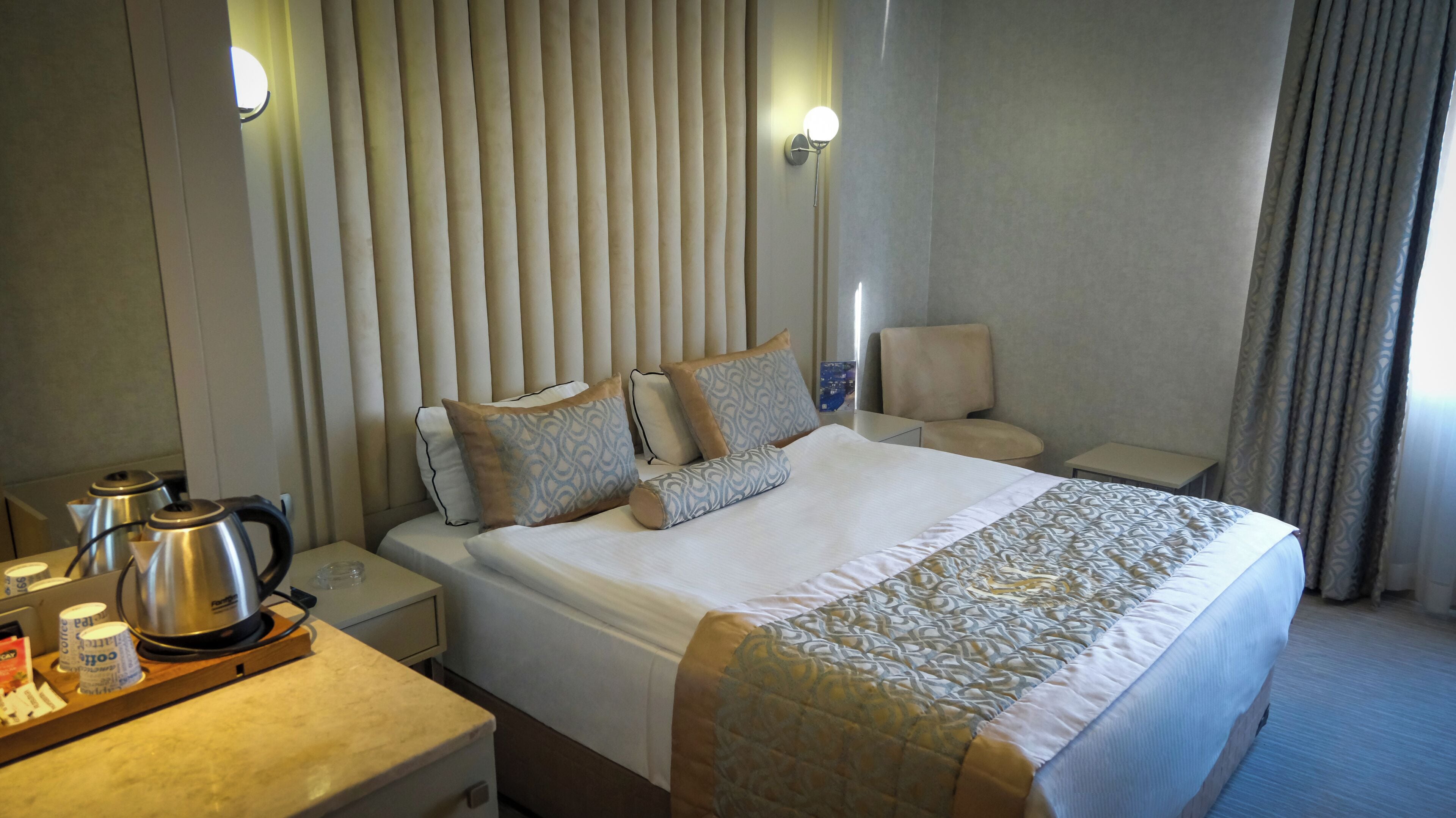 Een hotelkamer met een bed, een nachtkastje met een waterkoker, een stoel en een bureau met een lamp.