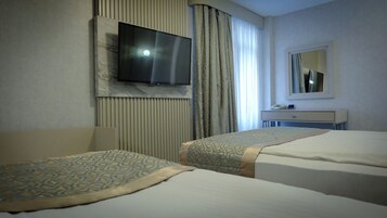 Habitación de hotel con dos camas, un televisor montado en la pared, una mesita de noche con teléfono y un espejo encima.