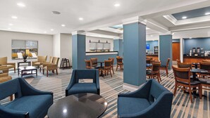 A hotel lobby with seating areas, a bar, and a view of the city.