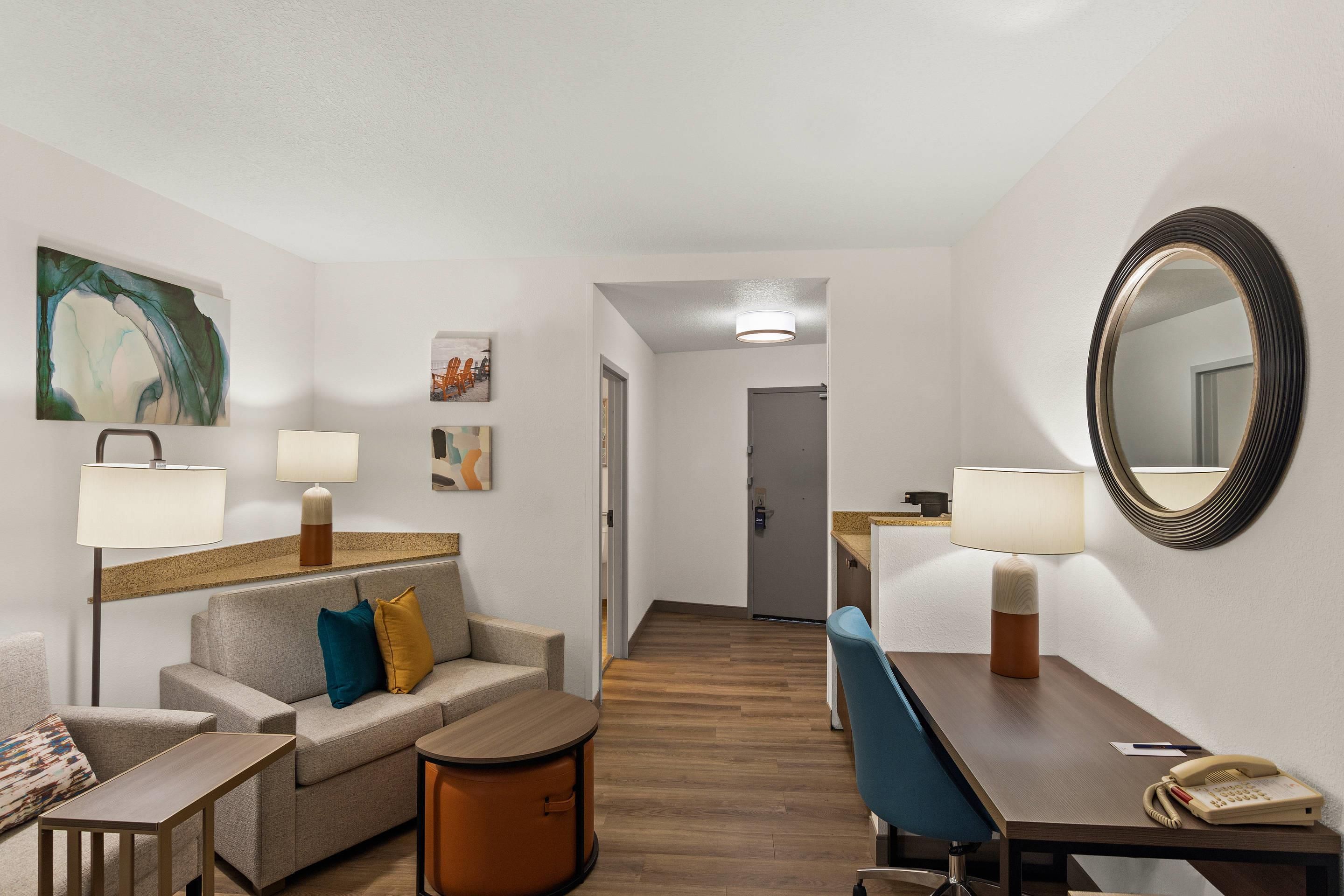 A hotel room with a sofa, armchair, small table, and a desk with a telephone.