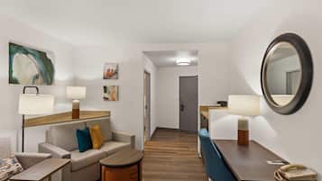 A hotel room with a sofa, armchair, small table, and a desk with a telephone.
