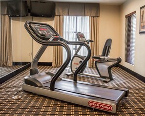 Une chambre d’hôtel équipée d’un tapis de course Star Trac, d’un deuxième appareil d’exercice, d’un téléviseur fixé au mur et d’une moquette à motifs.