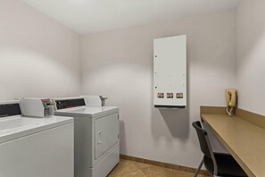 A laundry room with a washing machine, a dryer, a utility cabinet, and a telephone. - Comfort Suites Vero Beach I-95 (Vero Beach)