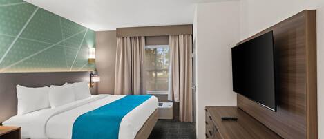 Habitación de hotel con cama, televisor de pantalla plana, escritorio y ventana con cortinas.