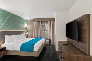 Une chambre d’hôtel équipée d’un lit, d’un téléviseur à écran plat, d’un bureau et d’une fenêtre avec des rideaux.