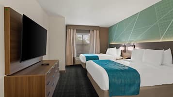 Habitación de hotel con televisor de pantalla plana, escritorio con control remoto, dos camas con cubrecamas color turquesa, ventana grande con cortinas y un diseño geométrico verde en la pared.
