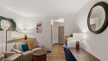 Habitación de hotel con sofá, una pequeña mesa redonda, una mesa de comedor, una silla, un espejo y dos lámparas fijadas a la pared.