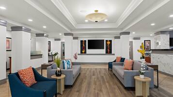 A modern hotel lobby with two sofas, a reception desk, and a large flat-screen TV mounted on the wall.