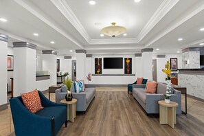 A modern hotel lobby with two sofas, a reception desk, and a large flat-screen TV mounted on the wall. - Comfort Suites Vero Beach I-95 (Vero Beach)