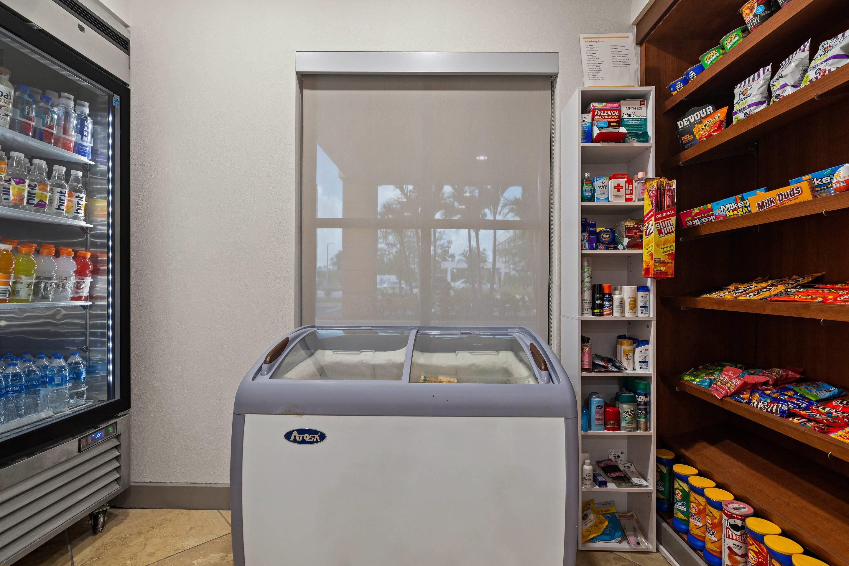 A small kitchenette area with a refrigerator, freezer, and shelves stocked with snacks and beverages.