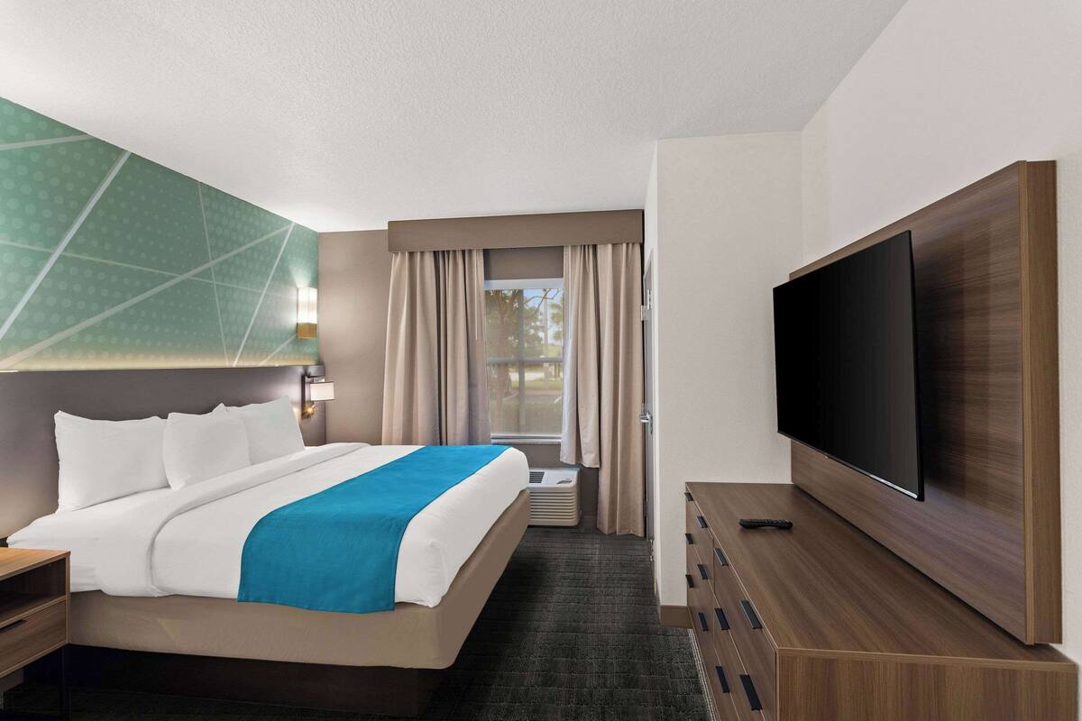 Une chambre d’hôtel avec un lit, une télévision, un bureau et une fenêtre avec des rideaux.