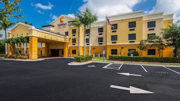 Un hotel con fachada amarilla, una bandera y un estacionamiento con flechas direccionales.
