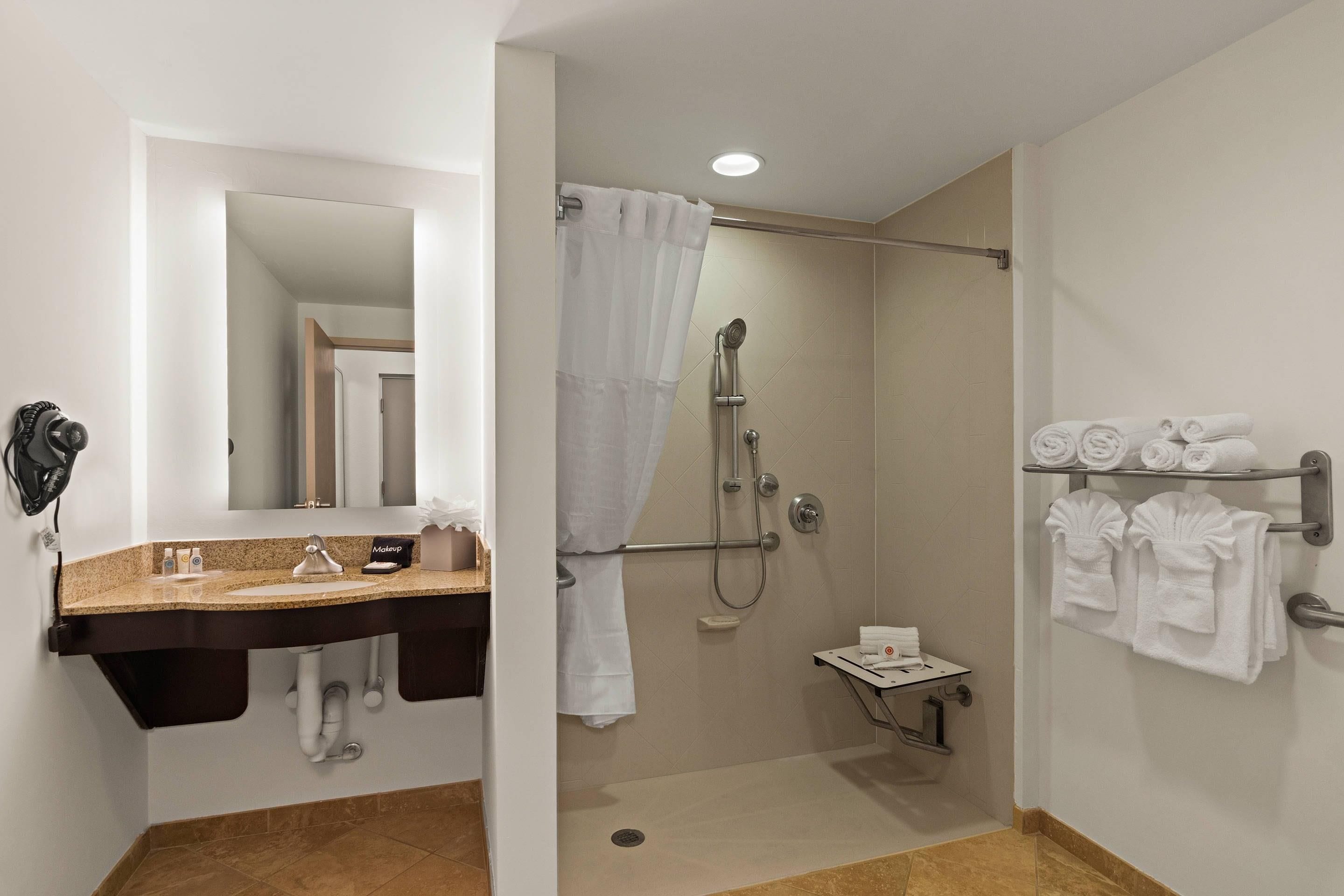 A bathroom with a shower, a sink, a mirror, and a towel rack.