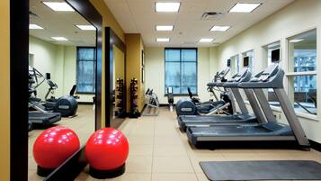 Une salle de sport équipée de tapis de course, de ballons d’exercice et d’un miroir.