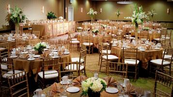 A banquet hall with round tables, gold chairs, and floral centerpieces.