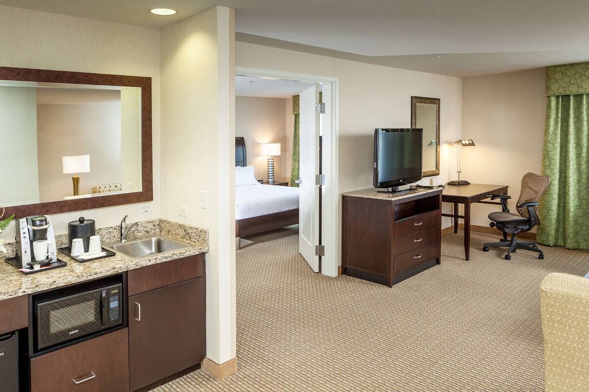 A hotel room with a kitchenette, a bed, a TV, a desk, and a chair.
