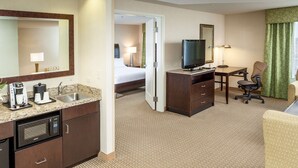Ein Hotelzimmer mit Küchenzeile, einem Bett, einem Fernseher, einem Schreibtisch und einem Sessel.