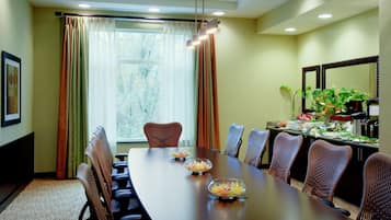 Un salón de conferencias con una larga mesa, sillas, una araña, cortinas y un ventanal con vistas a árboles.