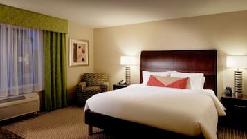 Habitación de hotel con una cama grande, dos lámparas de noche, una silla, un cuadro en la pared y una ventana con cortinas traslúcidas.
