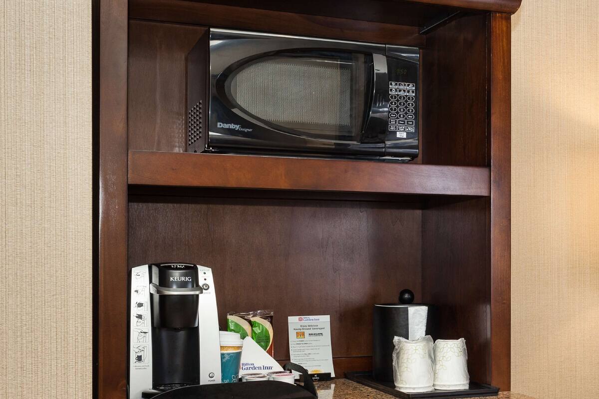 A kitchenette with a microwave, coffee maker, and coffee cups.
