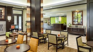 Eine Hotelhalle mit einer Rezeption, einer Sitzecke mit Tischen und Stühlen sowie einer Küche im Hintergrund.