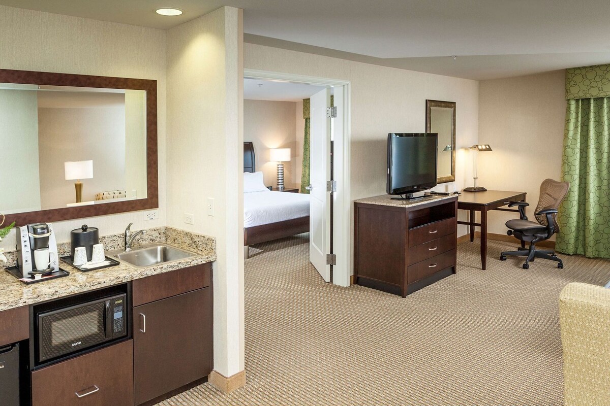 A hotel room with a kitchenette, a bed, a TV, a desk, and a chair.