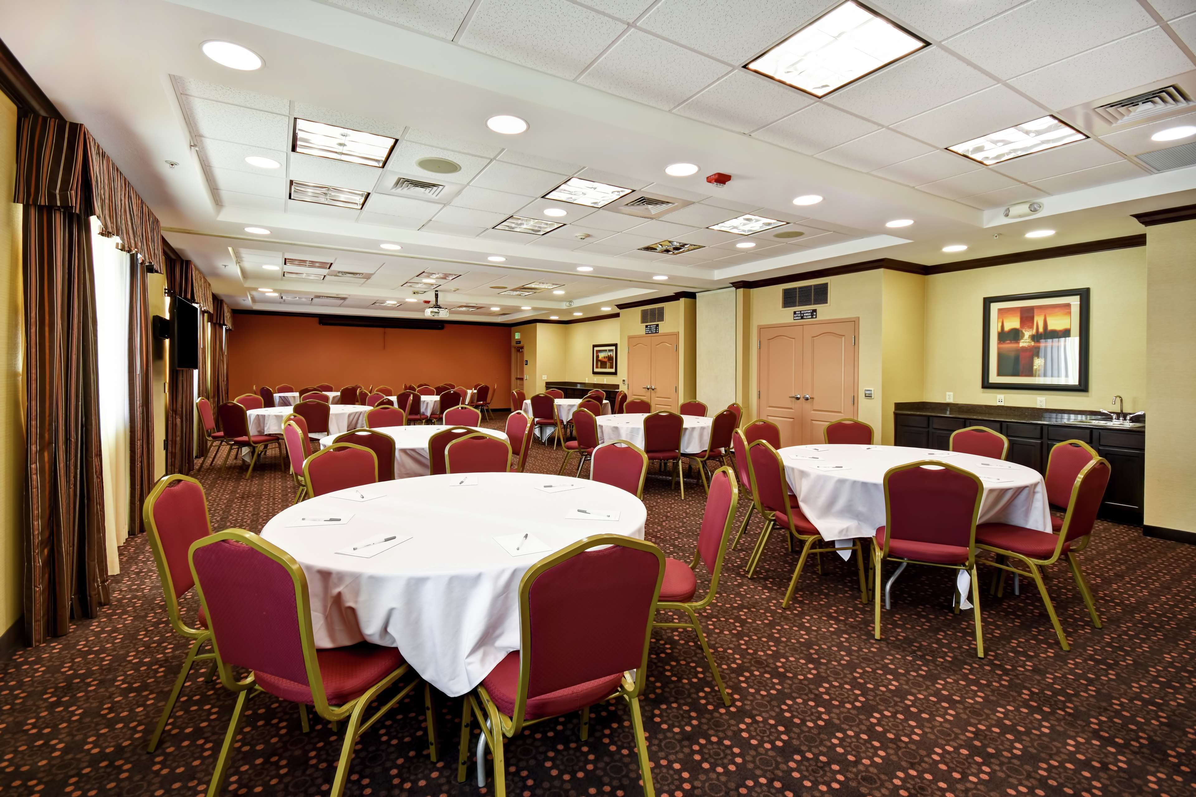 Une salle de conférence équipée de plusieurs tables rondes, de chaises rouges et d’un écran de projection.