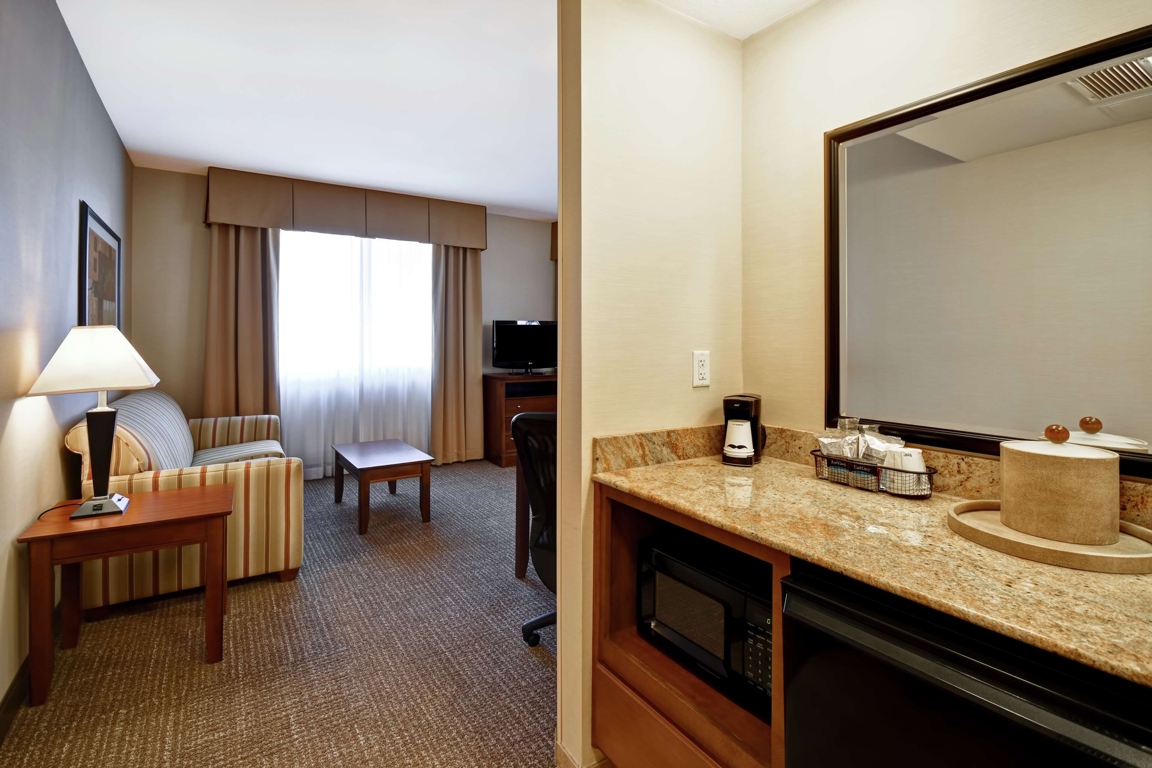 Une chambre d’hôtel équipée d’un canapé, d’une petite table, d’un bureau, d’une télévision, d’un four à micro-ondes, d’une machine à café et d’un grand miroir.