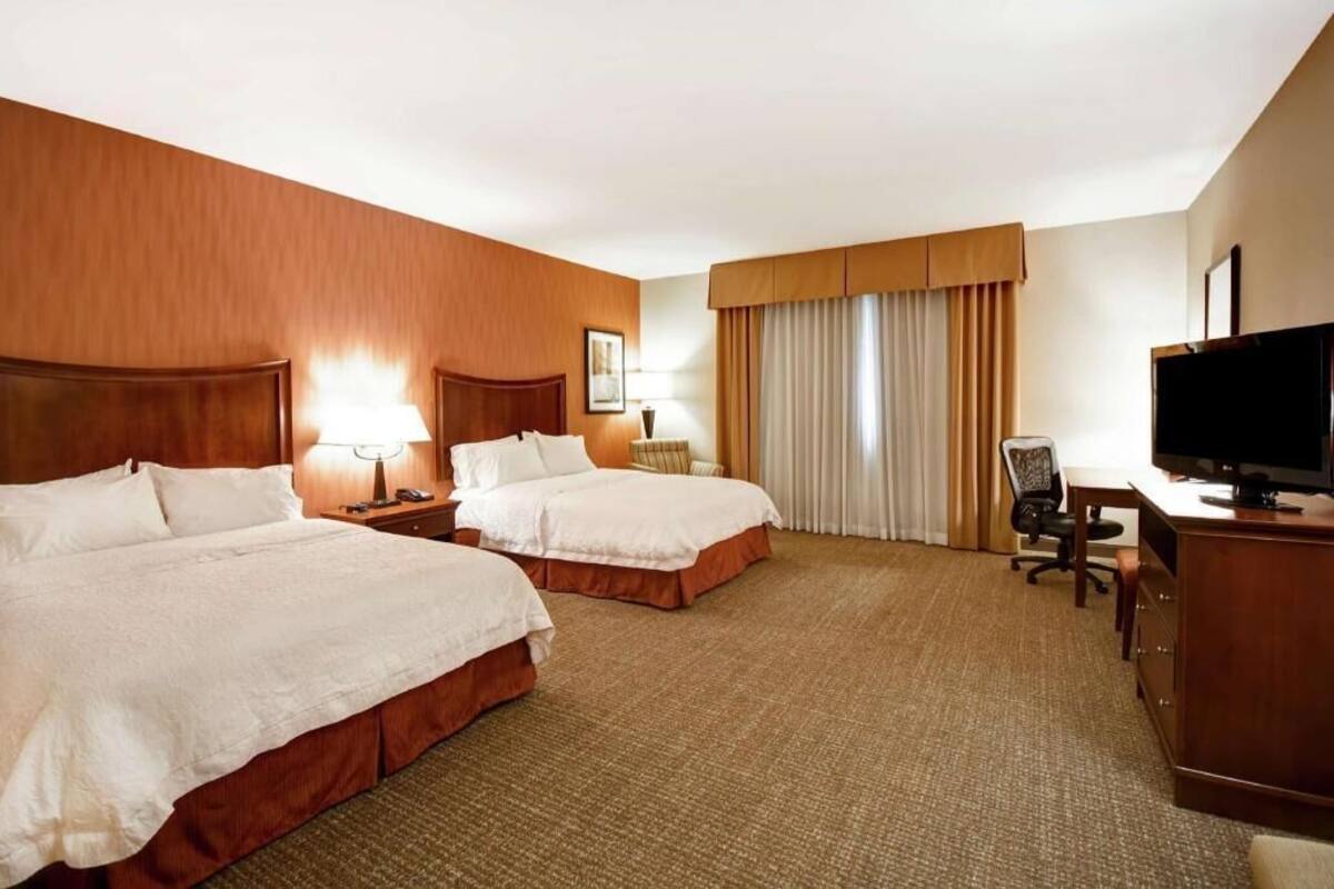 A hotel room with two beds, a desk, a television, and a window with curtains.