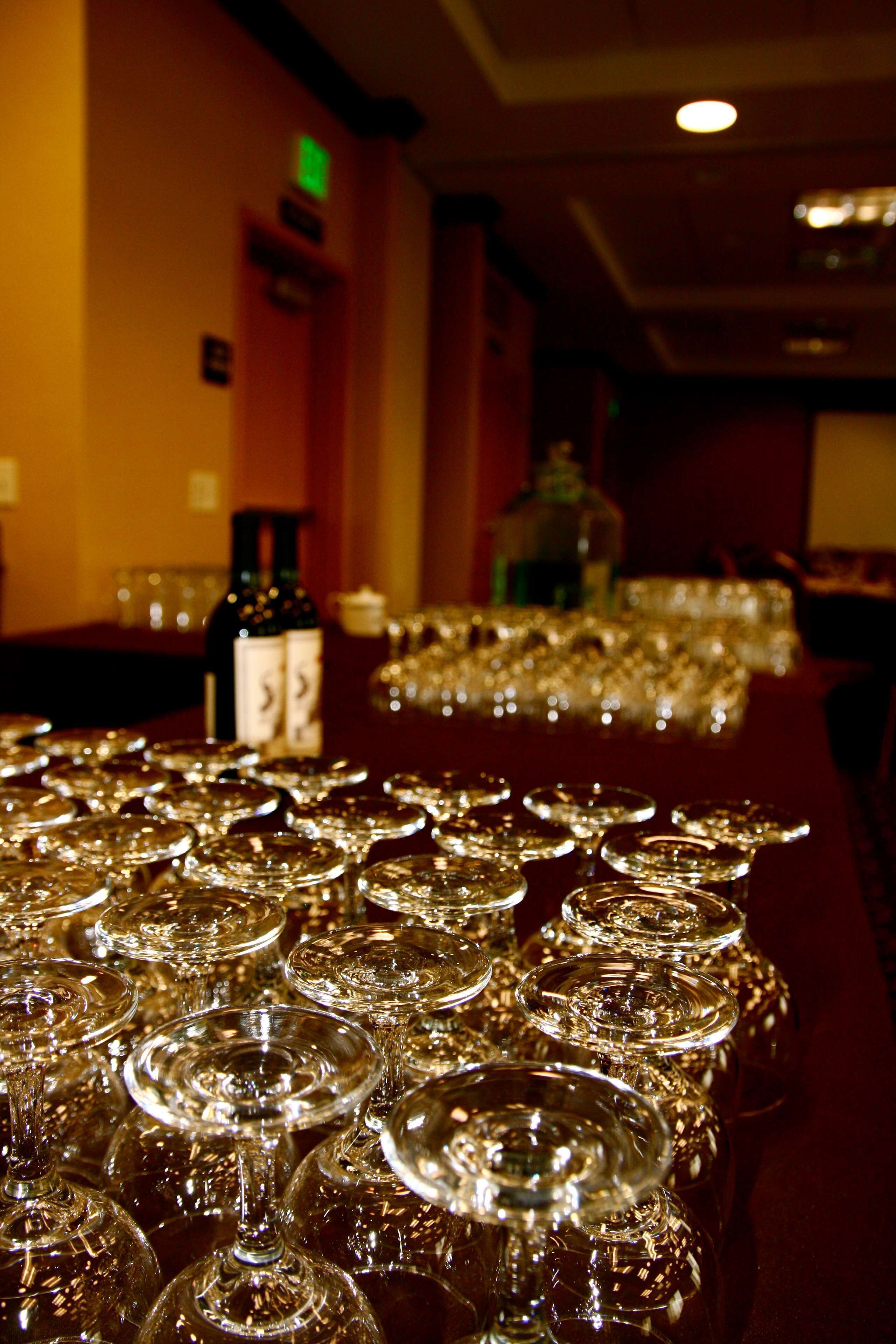 A table set with numerous wine glasses, a bottle of wine, and glasses on a table in a dimly lit room.