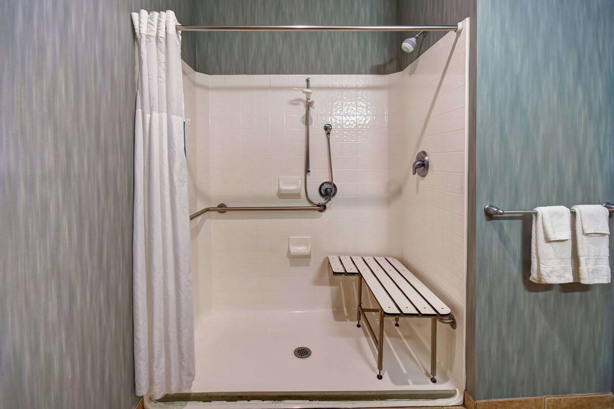 A shower with a bench, a towel rack, and a showerhead.