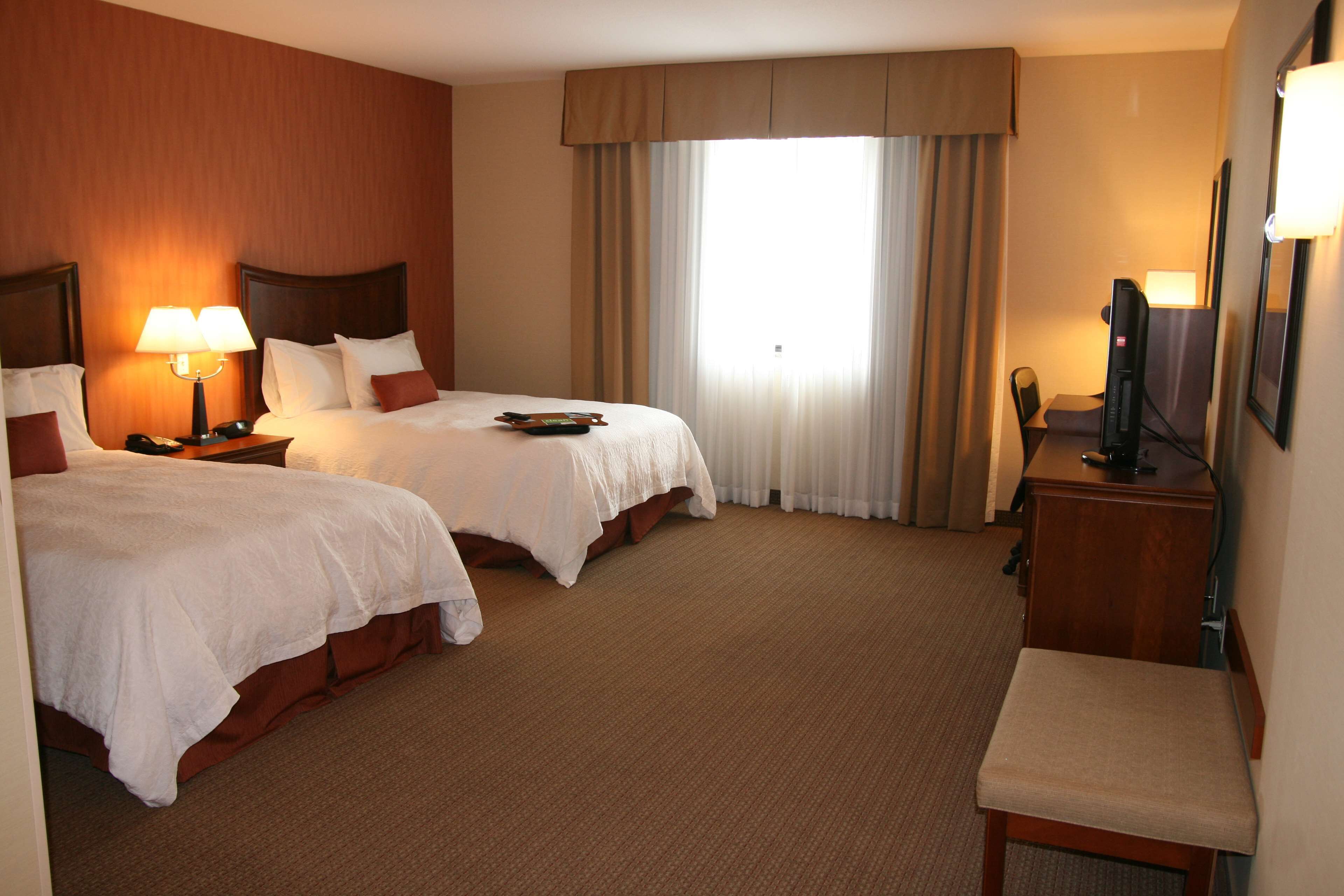 A hotel room with two beds, a desk, a chair, and a television.