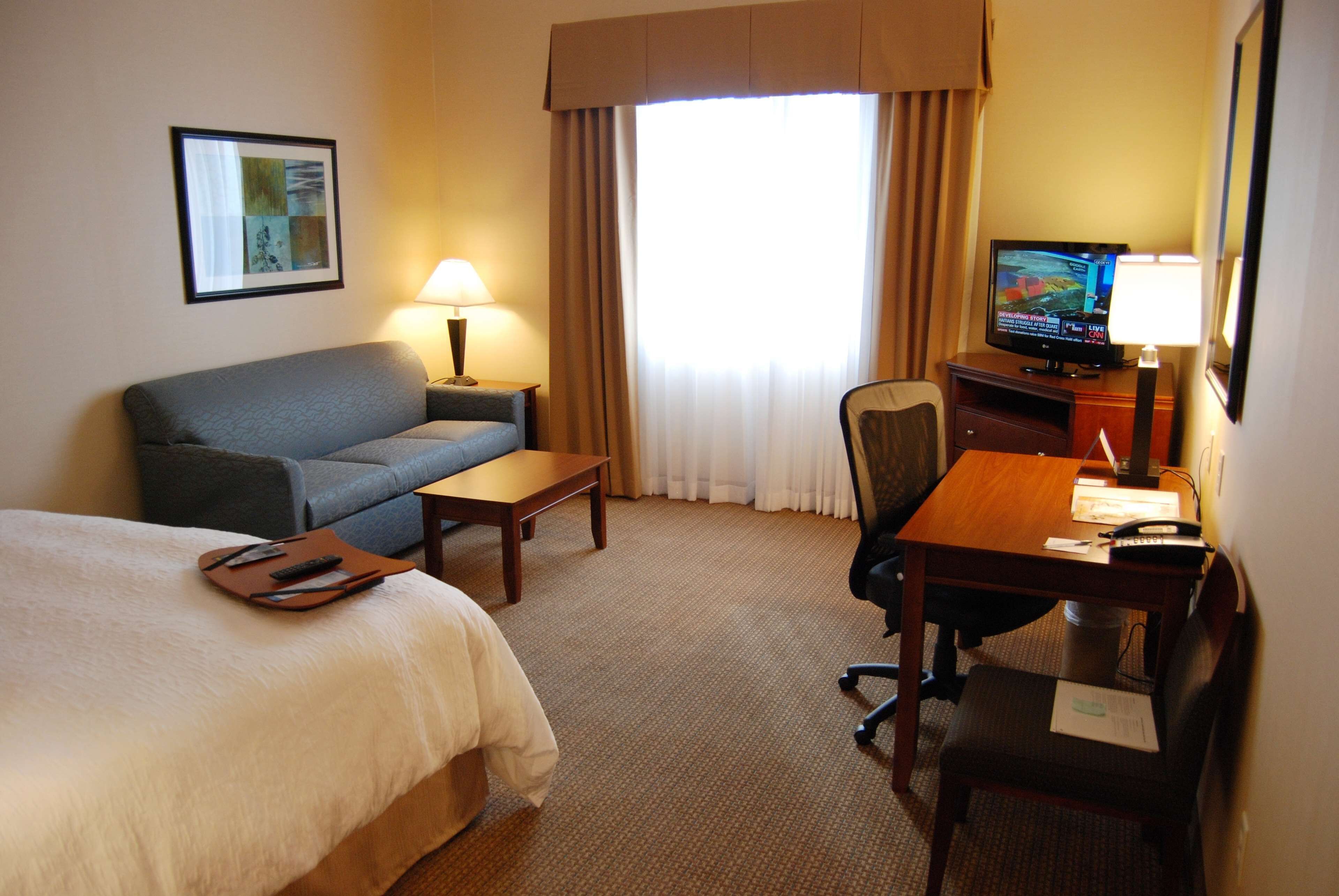 A hotel room with a bed, a sofa, a desk, a chair, a television, and a window with curtains.