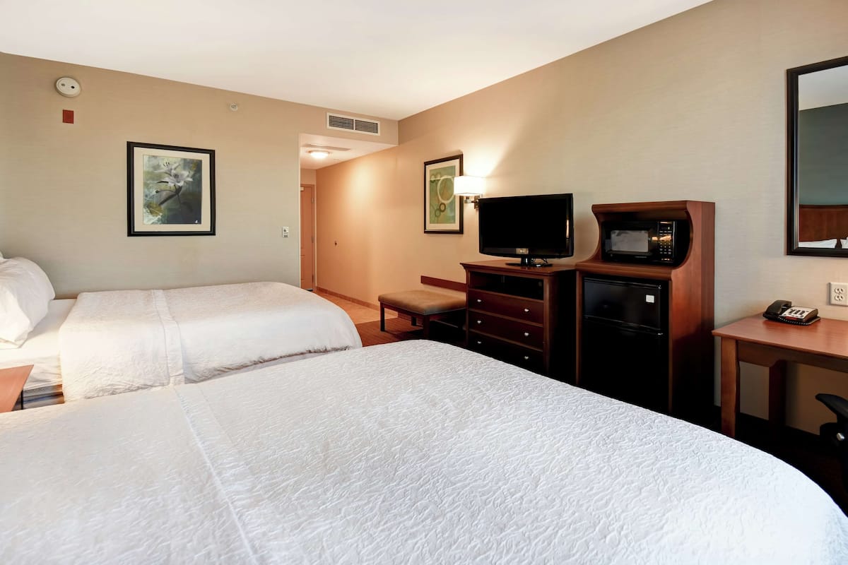 A hotel room with two beds, a desk with a television, a microwave, and a telephone.