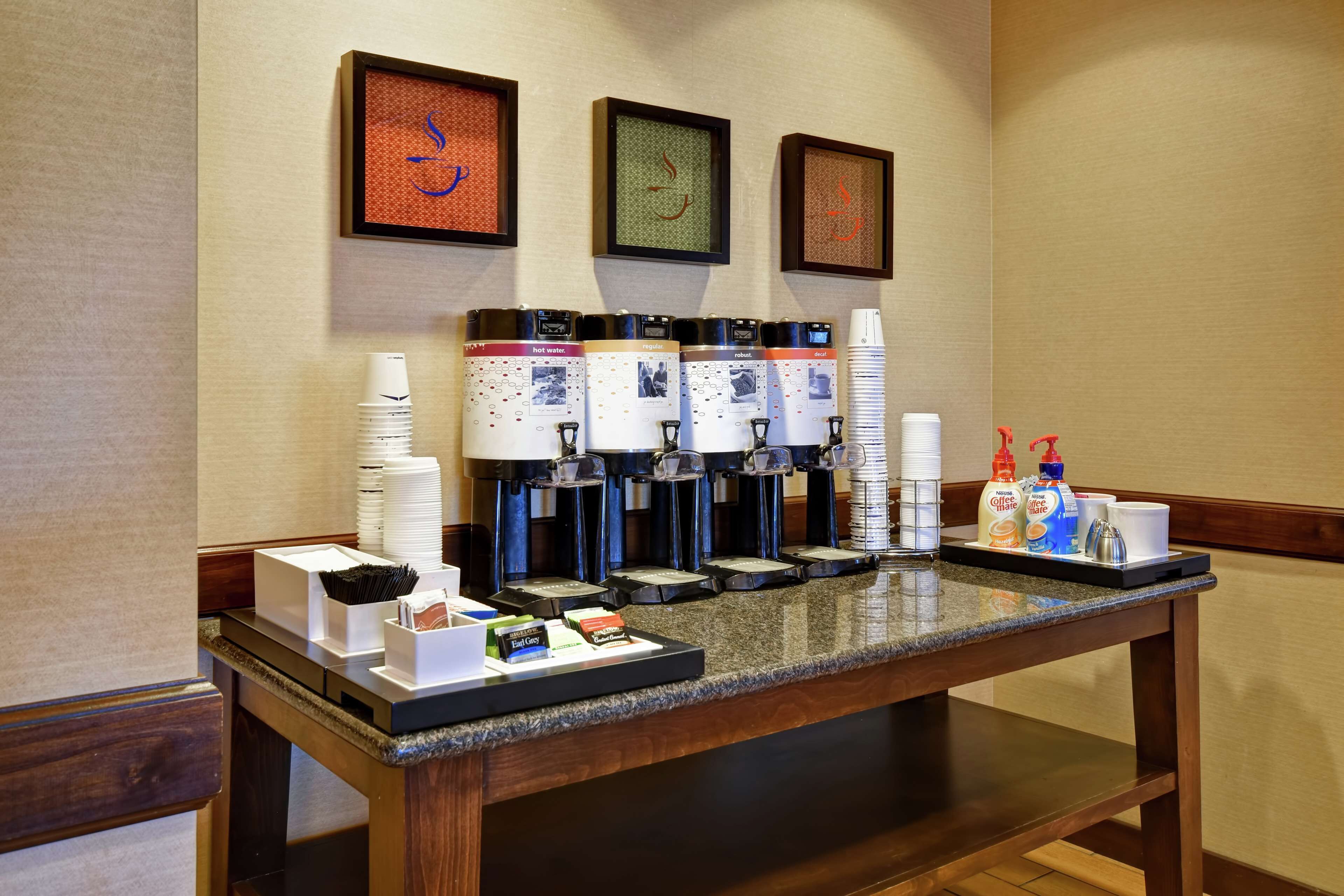 A coffee station with multiple dispensers, disposable cups, and a tray with condiments.