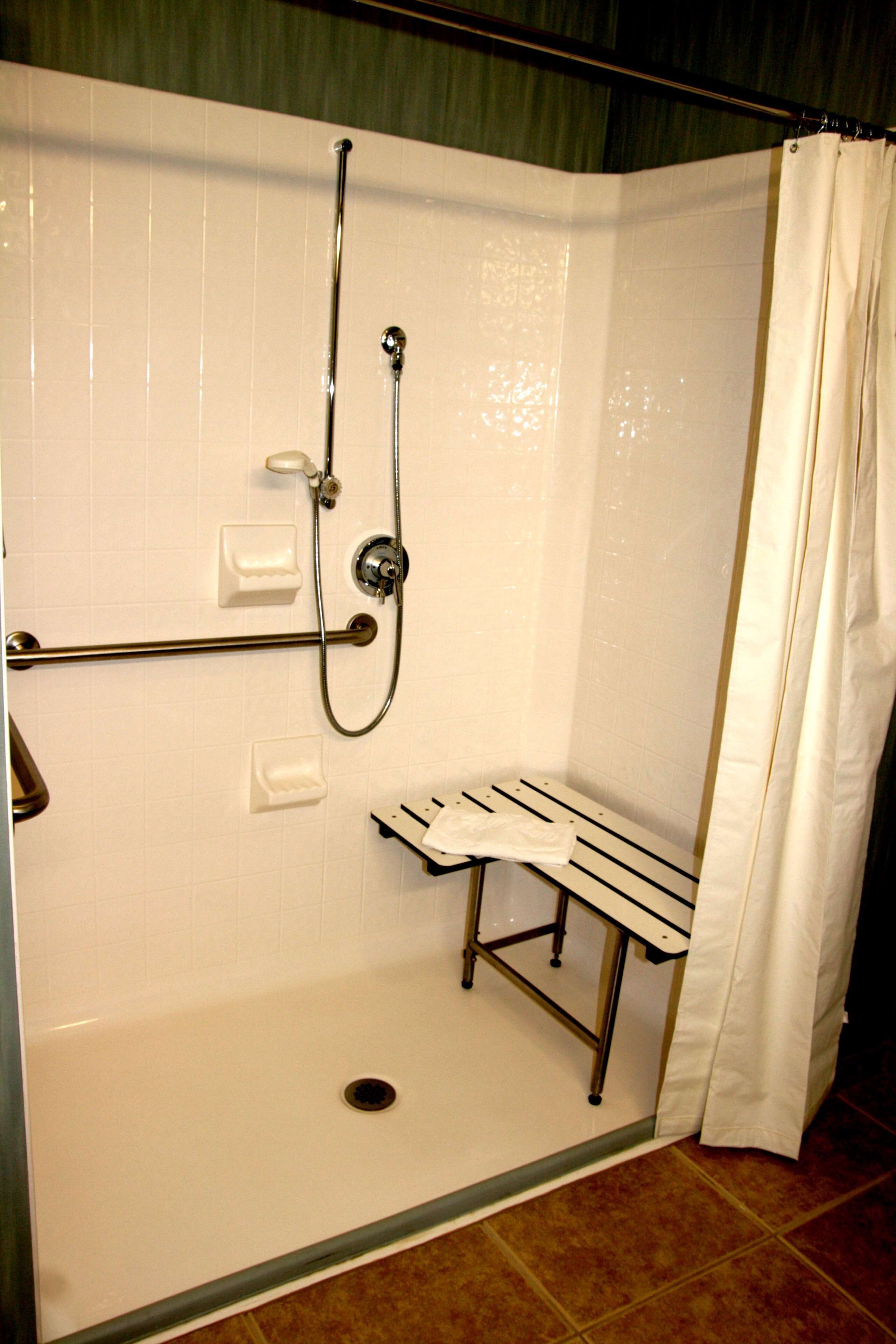 A shower area with a bench, a handheld showerhead, and a wall-mounted faucet.