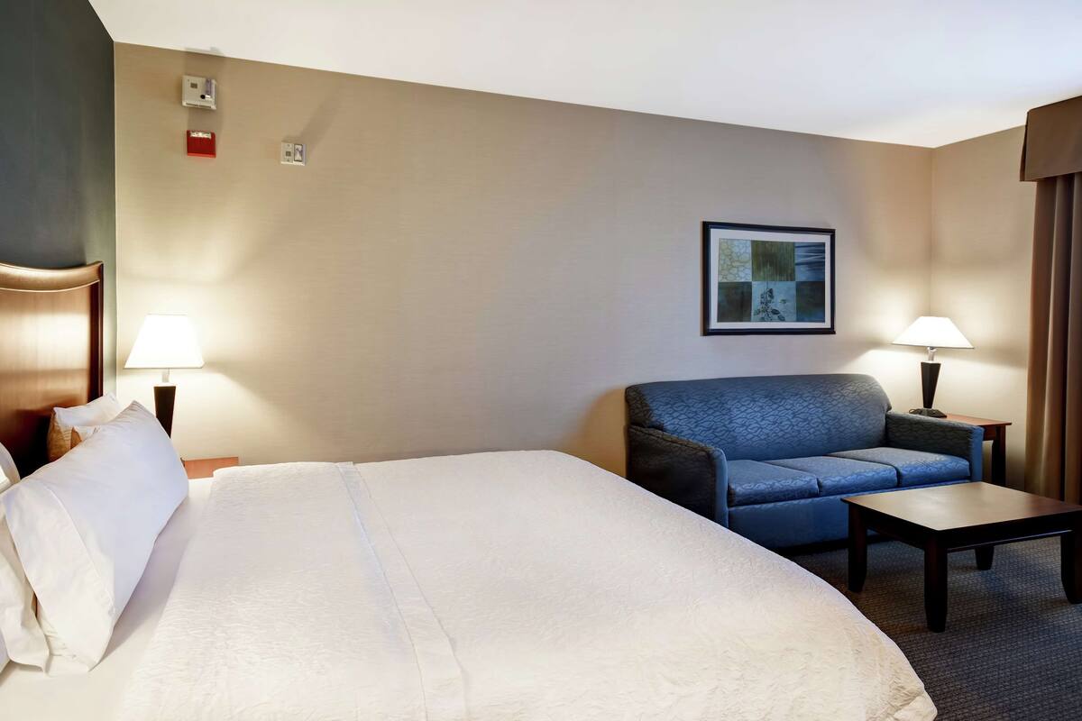 A hotel room with a large bed, a blue sofa, a small table, two lamps, and a framed picture on the wall.