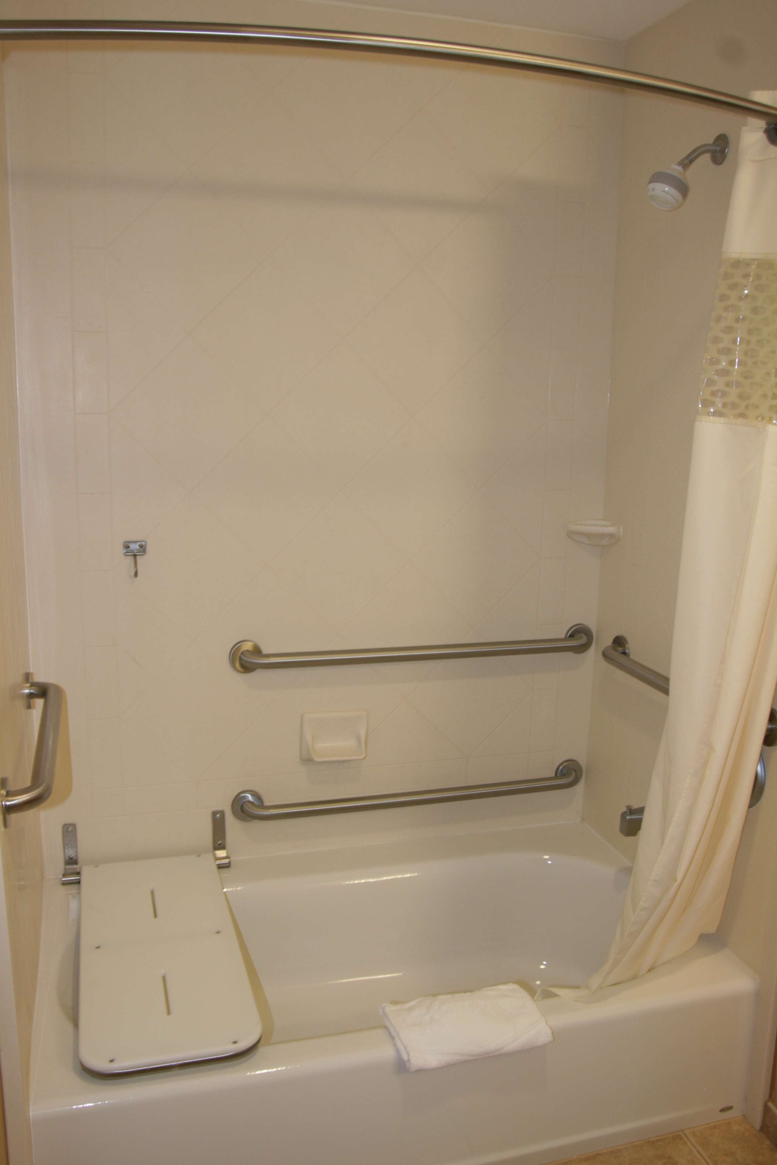 A bathroom with a bathtub, grab bars, a shower curtain, and a towel rack.