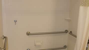 A bathroom with a bathtub, grab bars, a shower curtain, and a towel rack.