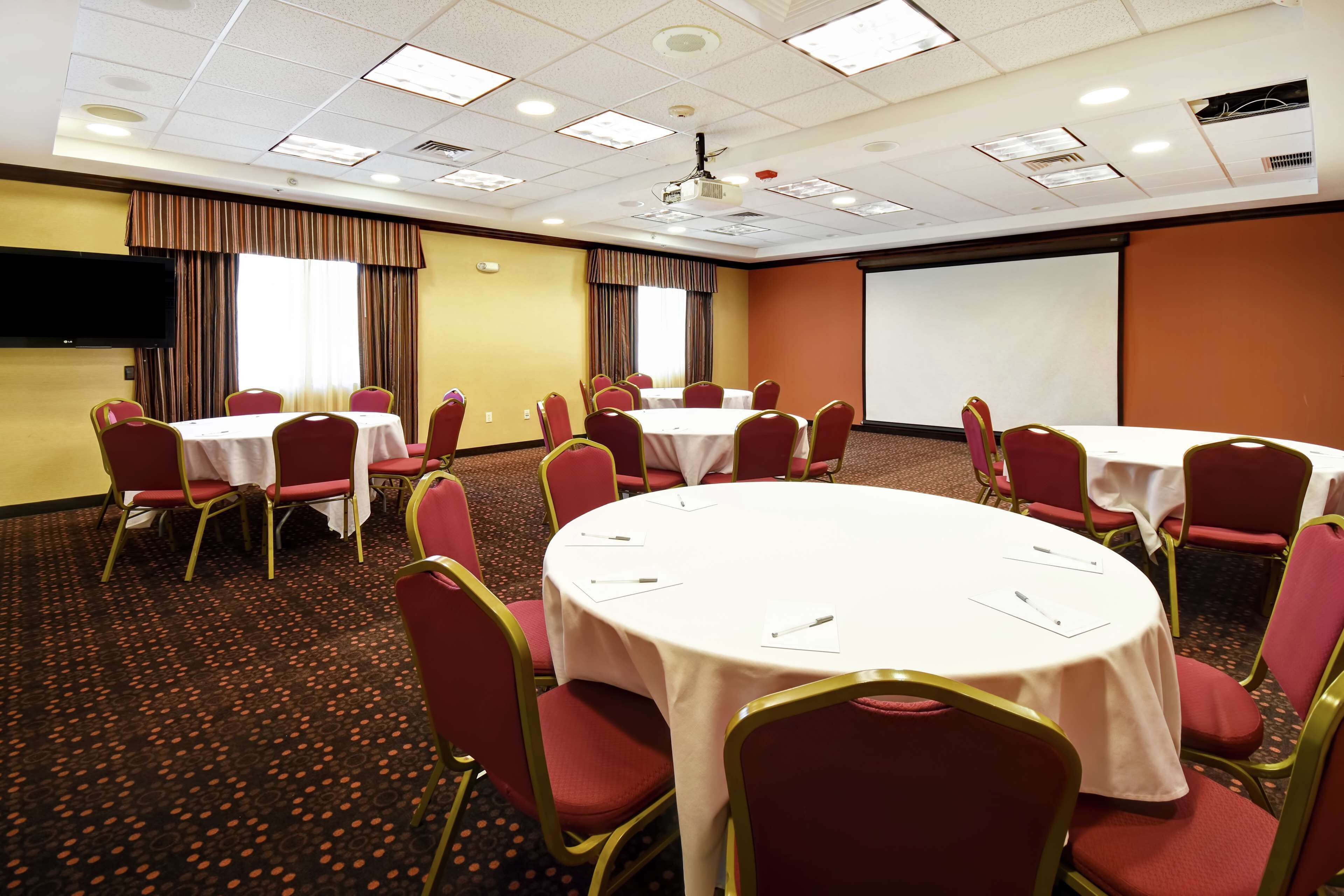 A conference room with multiple tables and chairs, a projector screen, and a large window with curtains.