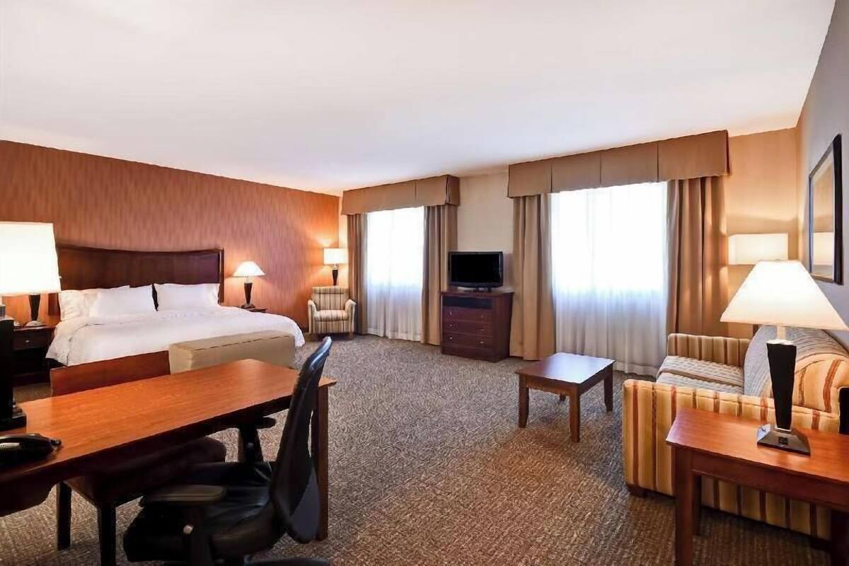 A hotel room with a bed, desk, chair, sofa, TV, and curtains.