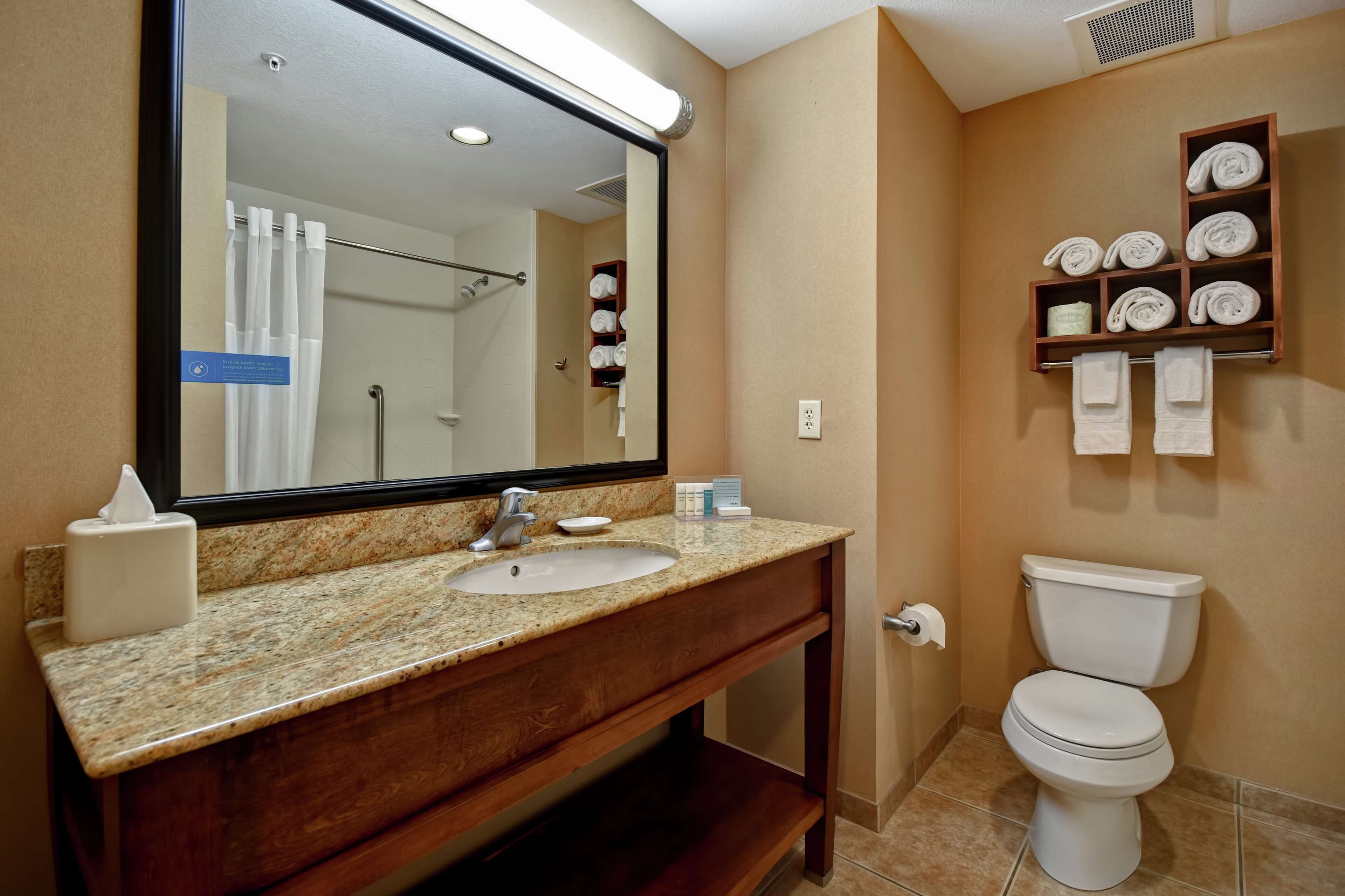 A bathroom with a granite countertop sink, a mirror, a toilet, and a towel rack with folded towels.