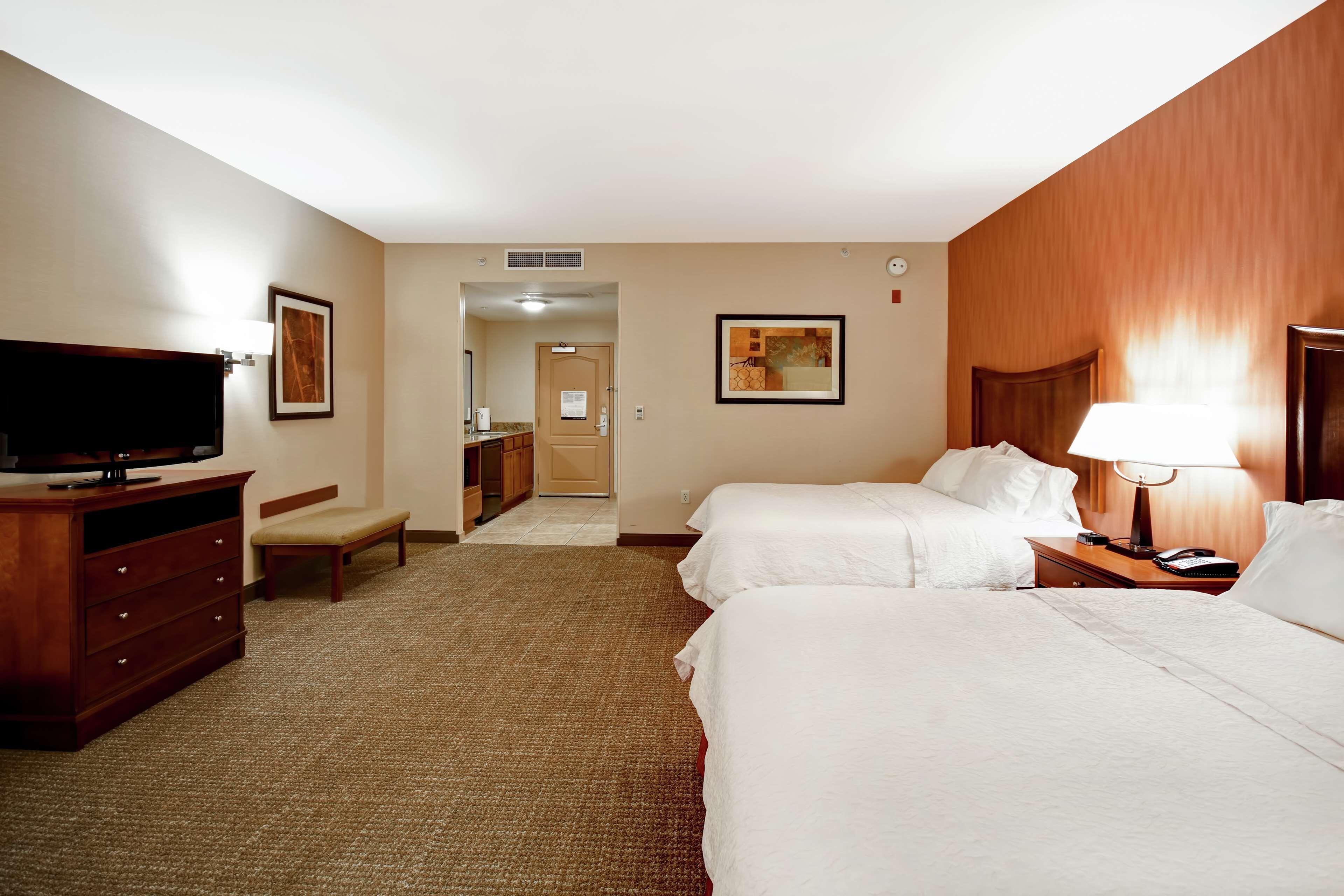 Habitación de hotel con dos camas, televisión, escritorio y baño visible a través de una puerta abierta.