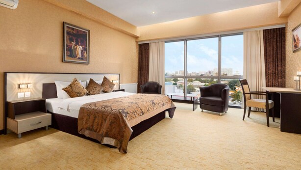 Une chambre d’hôtel avec un grand lit, un bureau, une chaise et une vue sur la ville grâce à de grandes fenêtres.