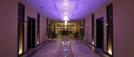 A hotel corridor with a central water feature, doors with decorative glass panels, and a ceiling light fixture.