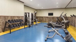 Une salle de sport équipée de matériel d’exercice, avec un porte-haltères et un téléviseur fixé au mur.