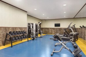 Een sportschool met trainingsapparatuur, een rek met gewichten en een televisie aan de muur.