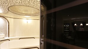 Une salle de bain avec une grande baignoire, un lavabo et un miroir. Le plafond est décoré d’un motif et un luminaire est installé au-dessus de la baignoire.
