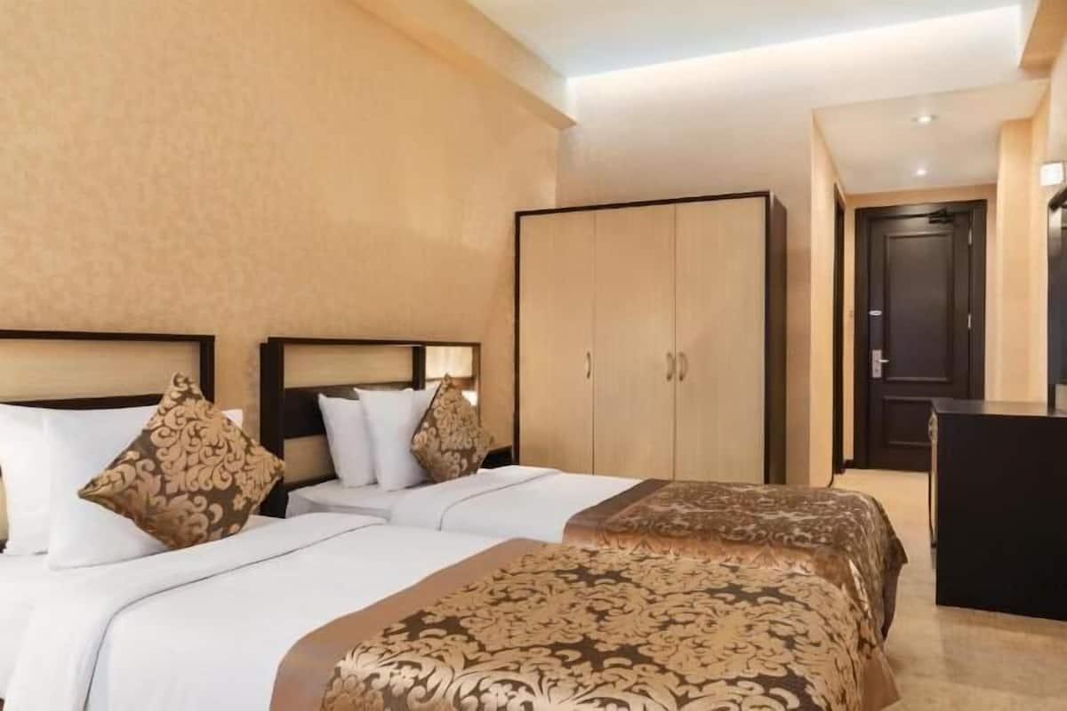 Ein Hotelzimmer mit zwei Betten, einem Kleiderschrank, einem Schreibtisch und einem an der Wand montierten Fernseher.