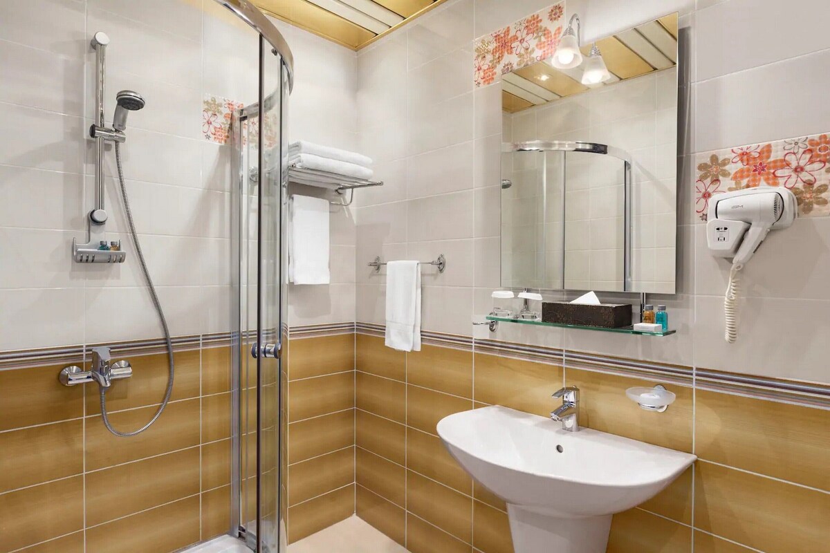 Een badkamer met een douchecabine van glas, een witte wastafel en een spiegel met een haardroger.